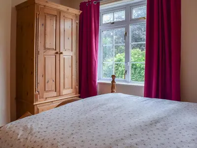 a bedroom with a bed and a window with pink curtains at Valentine Cottage in Keswick