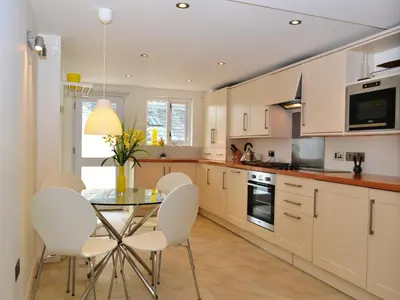 a kitchen with white cabinets and a glass table and chairs at 5 The Plosh in Keswick