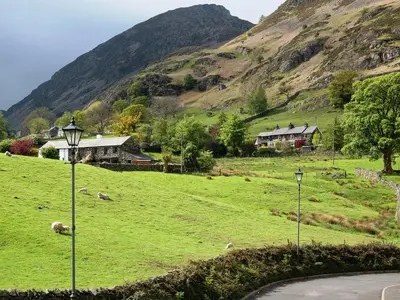 a field of green grass with a house and a mountain at Molly's Cottage in Glenridding