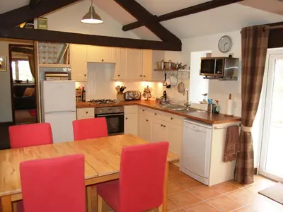 a kitchen with a wooden table and red chairs at Nuthatch Cottage in Westward