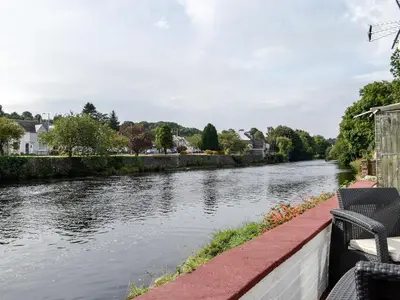 a view of a river with two chairs on a ledge at Minnow Cottage in Newton Stewart