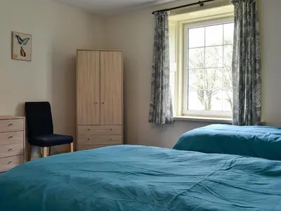 a bedroom with two beds and a chair and a window at Bonshawside Farmhouse in Kirtlebridge