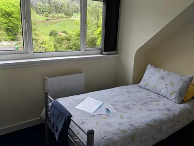 a bed with a book on it in a room with two windows at Barholm Accommodation in Creetown