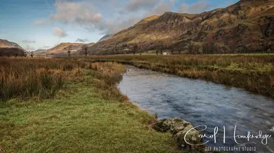a river in a field with mountains in the background at Red Rose Cottage in Cockermouth