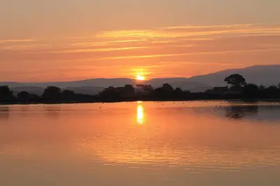 a sunset over a lake with the sun setting at Red Rose Cottage in Cockermouth