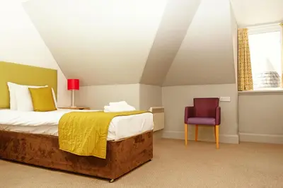 a bedroom with a bed and a red chair at The Portpatrick Hotel by Compass Hospitality in Portpatrick