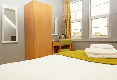 a bedroom with a bed and a desk and two windows at The Portpatrick Hotel by Compass Hospitality in Portpatrick