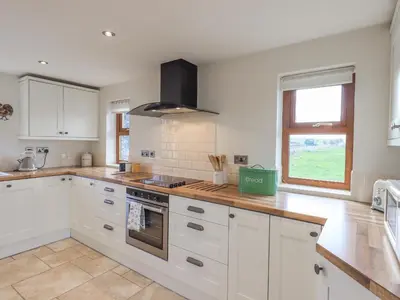 a kitchen with white cabinets and a stove top oven at South Milton Cottage in Glenluce