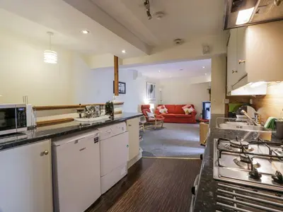 a kitchen with white cabinets and a living room at The Old Brewery Store in Gatehouse of Fleet