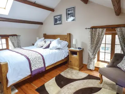 a bedroom with a bed and a chair and windows at Fell View Cottage in Bootle