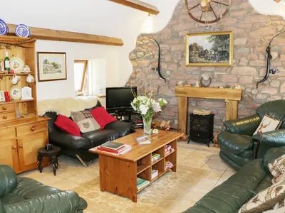 a living room with leather furniture and a stone fireplace at Piggery Cottage in Wigton