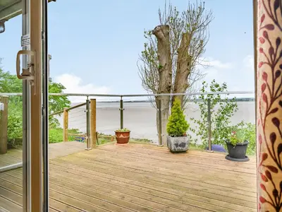 an open door to a deck with a view of the ocean at Solway Cottage in Bowness-on-Solway