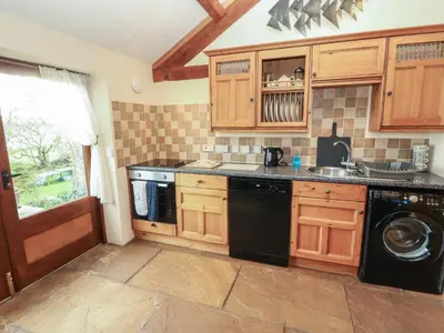 a kitchen with wooden cabinets and a black dishwasher at Sonya's Cottage in Anthorn