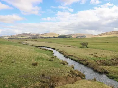 a winding river in a field with hills in the background at Sweetpea Cottage in Wiston