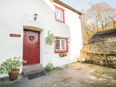 a white house with a red door and a stone wall at Stable End Cottage in Nether Wasdale