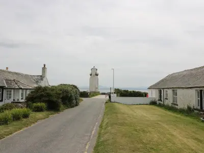 a road with houses and a lighthouse in the distance at Simmer Dim in Kirkbean