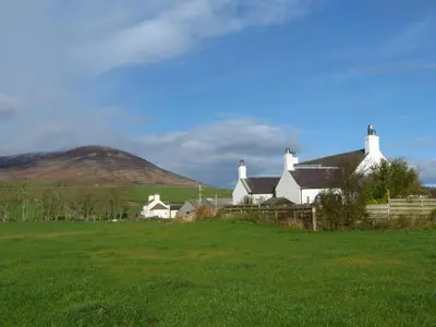 a house in a field with a hill in the background at Simmer Dim in Kirkbean
