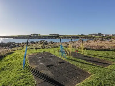 an empty swing set on the grass near the water at The Pink House in Isle of Whithorn