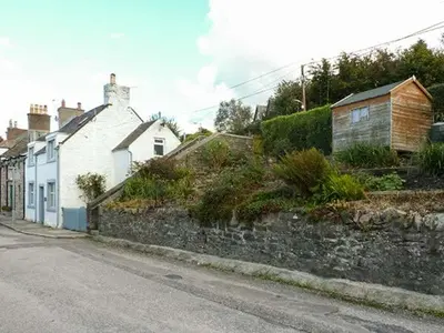 an empty street with houses and a stone wall at Nathaniel's Cottage in Kirkcudbright