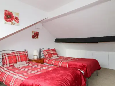 two beds in a white room with red sheets at Fountain Cottage in Keswick