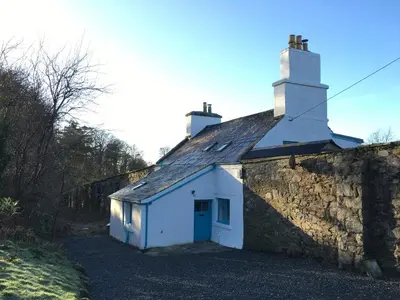 a white cottage with a chimney on top of a stone wall at Garden Cottage in Carsluith