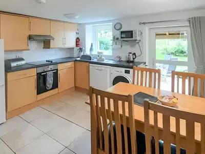 a kitchen with a wooden table and a dining room at Woodpecker Cottage in Westward