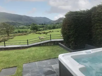 a hot tub with a view of a field and a cow on a bridge at The Hoggest in Threlkeld