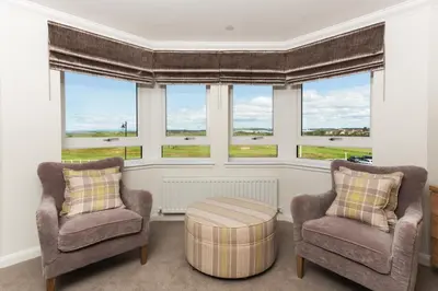 a living room with two chairs and a table and windows at Links View - Donnini Deluxe in Prestwick