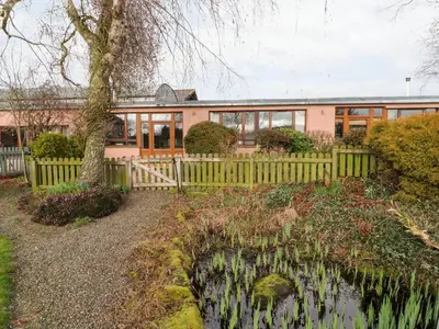 a house with a fence and a pond in front of it at Woodpecker in Ivegill