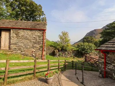 an old stone building with a fence and mountains in the background at The Hayloft in Keswick