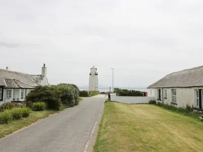 a road with houses and a lighthouse in the distance at The Bothy in Mainsriddle
