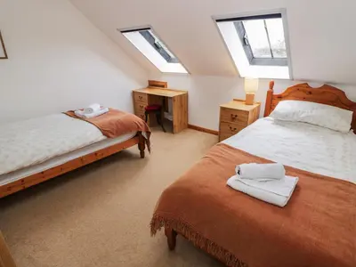 a bedroom with two beds and a desk and two windows at The Byre in Newton Stewart