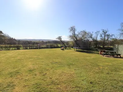 a large grass field with a picnic table and a bench at Hayloft Cottage in Wigton