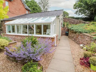 a house with a conservatory with flowers in the garden at North Lodge in Annan