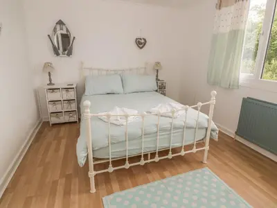 a bedroom with a white bed and a wooden floor at Wagtail Cottage in Mainsriddle