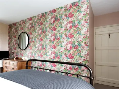 a bedroom with a floral wallpaper with a bed and a mirror at Stag Cottage in Penrith