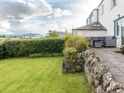 a garden with a stone wall and a house at Stag Cottage in Penrith