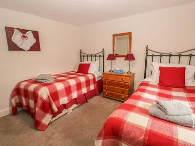 a bedroom with two beds and a dresser with a mirror at Rowan Cottage in Grasmere