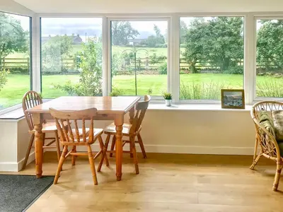 a dining room table and chairs in front of a window at Low Garth Cottage in Penruddock