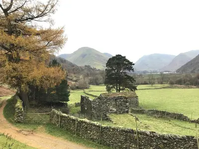 an old stone building in a field with mountains in the background at Low Garth Cottage in Penruddock