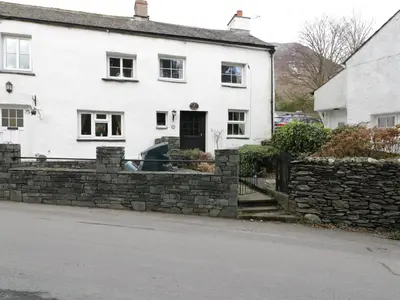 a white house with a stone fence in front of it at Nightingale Cottage in Threlkeld