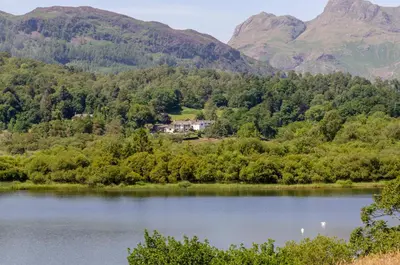 a house on the shore of a lake with mountains in the background at Eltermere Inn in Elterwater