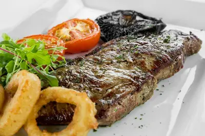 a piece of steak with onion rings and vegetables on a plate at The Greenhill Hotel in Wigton