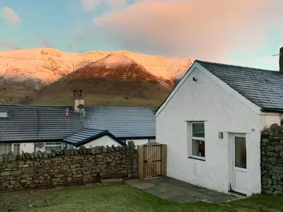 a white house with a stone fence and a mountain at Katellen Cottage in Threlkeld