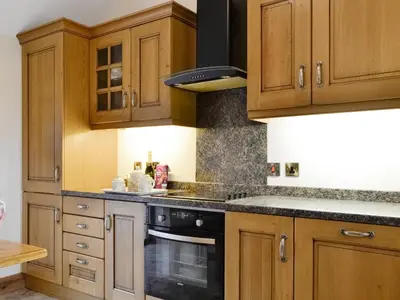 a kitchen with wooden cabinets and a stove top oven at The Old Byre in Dearham