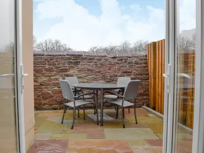 a table and chairs on a patio with a stone wall at Brodie Cottage in Aspatria