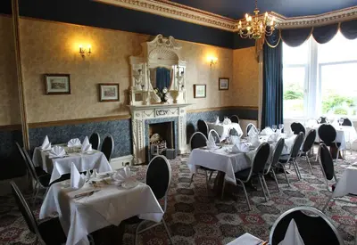 a dining room with tables and chairs and a fireplace at Cressfield Country House Hotel in Ecclefechan