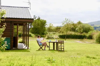 a woman sitting at a table in a garden at Lapwing, Skylark & Curlew Seaside Chalets in Kirkbean