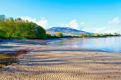 a beach with a body of water and a mountain at Shore Cottage in Dumfries