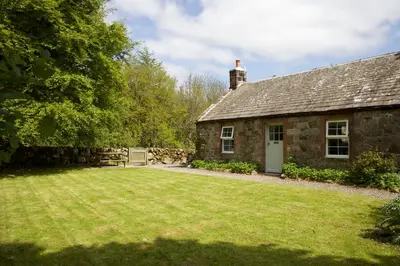 an old stone house with a large yard at Little Dunbar Cottage in Kirkbean